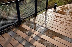 Wet wooden ground path on park after rain isolated on horizontal ratio steel iron metal net railing with natural evening sun light background. photo