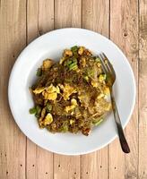 Stir fried sweet soy sauced rice noodle vermicelli with scrambled eggs and long beans in plate from above top view angle isolated food photography on vertical wooden background. Bihun goreng telur. photo