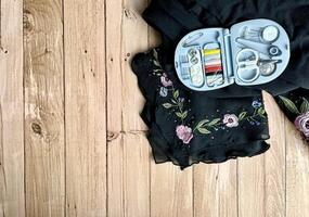 Travel size compact sewing tailoring kit on black flower clothing fabric. Object photography isolated on horizontal wooden table desk background with empty copy space for texts. photo