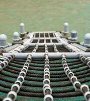 Black rope with net shapes tied on steel structure isolated on vertical ratio first person pov above angle view outdoor playground green flooring environment. photo