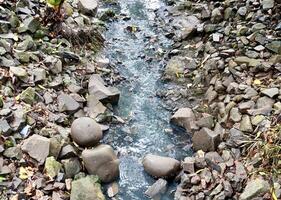 Narrow rough water stream flow between rock stones and pebbles isolated on horizontal ratio background on outdoor environment background photography. photo