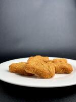 Deep fried crispy and delicious chicken nugget dish on white plate. Food photography isolated on vertical dark black background with empty copy space for text. photo