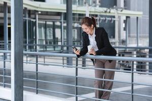 Asian businesswoman drinks coffee and discusses work on the phone in the hallway outside the office. photo