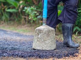 Man holding a cement rod for hammering to adjust the asphalt surface for the walkway. Close-up photo. Constructed from asphalt. Space for text photo