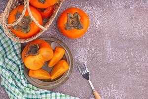 Top view of ripe persimmons with cloth and cutlery on a gray stone background with copy space for text. Concept of health fruit photo