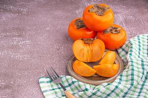 Fresh ripe persimmons with slices of persimmon on a plate with cutlery and whole fruit on gray stone background. Space for text. Close-up photo. Concept of health fruit photo