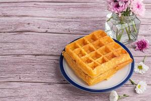 The waffle or Honeycomb dessert is placed on a white plate with flowers on a wooden table. Top view with space for text. Concept of dessert and relaxation photo