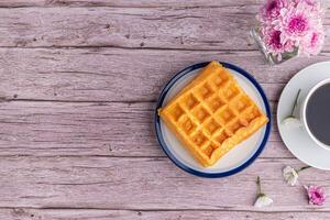 The waffle or Honeycomb dessert is placed on a white plate and a white cup of coffee with flowers on a wooden table. Top view with space for text. Concept of dessert and relaxation photo