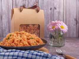 Sweet and sour crispy noodles or Mee krob in the Thai language on a dish with cloth, vase placed on a gray stone background. Side view with copy space for text photo