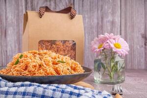 Sweet and sour crispy noodles or Mee krob in the Thai language on a dish with cloth, vase placed on a marble table. Side view with copy space for text photo