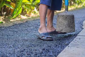 Man holding a cement rod for hammering to adjust the asphalt surface for the walkway. Close-up photo. Constructed from asphalt. Space for text photo