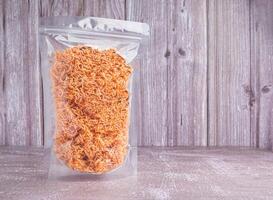 Side view of sweet and sour crispy noodles or Mee krob in the Thai language in a clear package placed on gray stone with wooden wall background. Space for text. Snack ready to eat photo