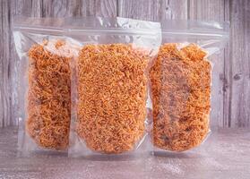 Side view of sweet and sour crispy noodles or Mee krob in the Thai language in a clear package placed on gray stone with wooden wall background. Space for text. Snack ready to eat photo