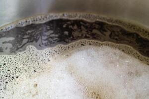 Close-up of craft beer and foam in a fermentation container. Process of making home beer from malt. Craft beer from barley and dark malt. Selective focus photo