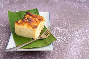 Thai custard cake on banana leaf and spoon on a white plate with a stone background. Egg custard with mung bean flour. Thai dessert is famous. Space for text photo