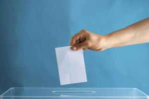 Closeup of a hand casting a white paper ballot into a transparent box on a blue background photo
