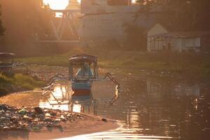 A traditional boat moored in a polluted river near riverside buildings in the serene morning light with golden sunlight, creating a tranquil atmosphere. photo