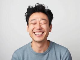 Happy Young Asian Man Smiling with Eyes Closed in a Casual Blue Sweater on a White Background, Expressing Joy and Contentment photo