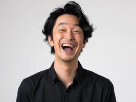 Young Asian Man in Black Shirt Laughing Out Loud on Plain Background, Expressing Joy and Amusement photo
