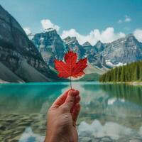 Red maple leaf in hand against the backdrop of a landscape with a lake and mountains. photo