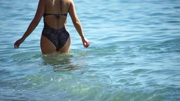 Back View at Young Happy Carefree woman in swimsuit jogs over sand in shallow waterline. Small waves splashes over legs of young woman running along seashore. Concept of summer vacation. video