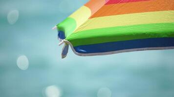 Rainbow colored beach umbrellas or parasols against blue sea during a sunny day on a beach. Symbol of vacations, relax, summer. Colorful umbrellas from the sun stand on the beach. Slow motion. video