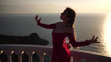 Closeup portrait of sensual young brunette woman in red dress, looking up in sky, happily outdoors isolated at blurry sea background natural bokeh in soft warm sunset backlight. video
