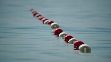 Orange and white safety buoys on a rope floating in the sea on a sunny day, close up. Fencing of the swimming area on the beach. Vacation, travel and holiday concept. Slow motion video
