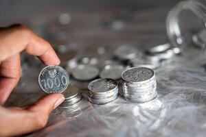 Hand holding 1000 Rupiah coin with stacks of coins photo