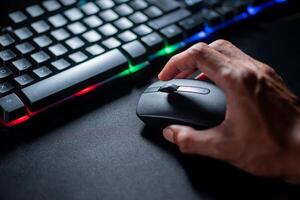 Hand using computer mouse next to RGB keyboard photo