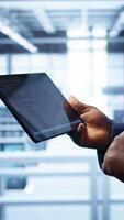 Vertical Engineer in high tech facility using tablet to patch network issues leading to slow data transfer rates. Close up of worker fixing errors affecting servers performance and connectivity, camera B video