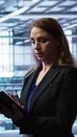 Vertical Meticulous technician doing checkup, inputting data on tablet of needed fixes in server hub housing advanced data storage infrastructure supporting critical IT workloads, camera B video