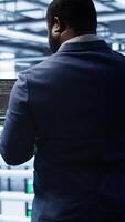 Vertical African american admin in data center running error checking utilities on tablet to fix hardware bugs. IT expert in server hub workspace looking for issues affecting mainframes performance, camera B video