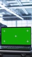 Vertical Green screen laptop used by engineers monitoring server room, doing checkup. Focus on chroma key notebook used by IT support employee working in data center facility, camera B close up video