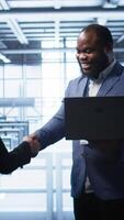 Vertical African american admin greeting inspector arriving in data center to supervise operations. IT expert in server hub workspace doing hand shake with supervisor monitoring performance, camera B video