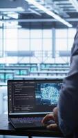 Vertical Software developer in data center using artificial intelligence computing simulating human brain. IT support staff member working on notebook with AI machine learning algorithms, camera B video