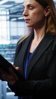 Vertical Admin in server room checks recovery plan on tablet, monitoring equipment energy consumption. IT professional uses notebook in data center workplace, ensuring rigs are functioning optimally, camera B video