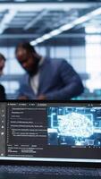 Vertical Close up of laptop with AI technology used to sustain data center hardware. Focus on notebook used by server room programmers in background using artificial intelligence tech, camera B video