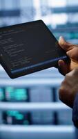 Vertical Engineer in high tech facility using tablet to patch network issues leading to slow data transfer rates. Close up of worker fixing errors affecting servers performance and connectivity, camera A video