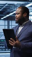 Vertical Software engineer in data center runs error checking utilities on tablet to fix problems. IT specialist looking for network issues affecting rigs performance using digital device, camera A video