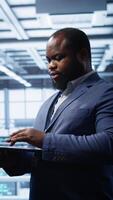 Vertical Programmer in data center typing on laptop, running error checking utilities. IT professional in server room looking for network issues affecting rigs performance using digital device, camera B video