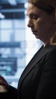 Vertical Meticulous technician doing checkup, inputting data on tablet of needed fixes in server hub housing advanced data storage infrastructure supporting critical IT workloads, camera A video