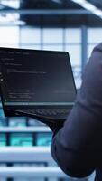 Vertical Programmer doing yearly maintenance checkup using laptop to prolong data center electronics life span. IT professional in server farm monitoring server infrastructure using notebook, camera A video