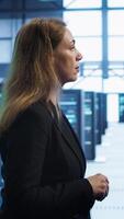 Vertical Engineer walking in data center workspace, monitoring systems to identify root cause of errors. Woman in server hub establishment doing diagnosis, looking for equipment bugs needing repairs, camera A video