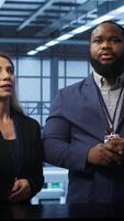 Vertical Admin and coworker looking at holograms in data center, doing swiping motions hand gestures. IT support staff members interacting with augmented reality AI visualization in server hub, camera A video