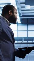 Vertical Admin doing yearly checkup using notebook to prolong data center electronics life span and avoid downtime. Man walks in server room, monitoring server infrastructure components using laptop, camera A video