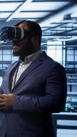 Vertical African american developer immersed in virtual reality at data center, doing units maintenance. Technician using VR headset to optimize servers performance, checking operations, camera A video