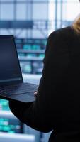 Vertical System administrator in server farm using laptop to patch network issues leading to slow data transfer rates. IT support staff member in data center fixing errors affecting supercomputers, camera A video