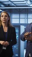 Vertical Team of admins in high tech data center looking at hologram visualization. Engineer and coworker working on securing serves using AR tech, preventing hacker attacks, camera A video
