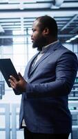 Vertical Software engineer in data center runs error checking utilities on tablet to fix problems. IT specialist looking for network issues affecting rigs performance using digital device, camera B video